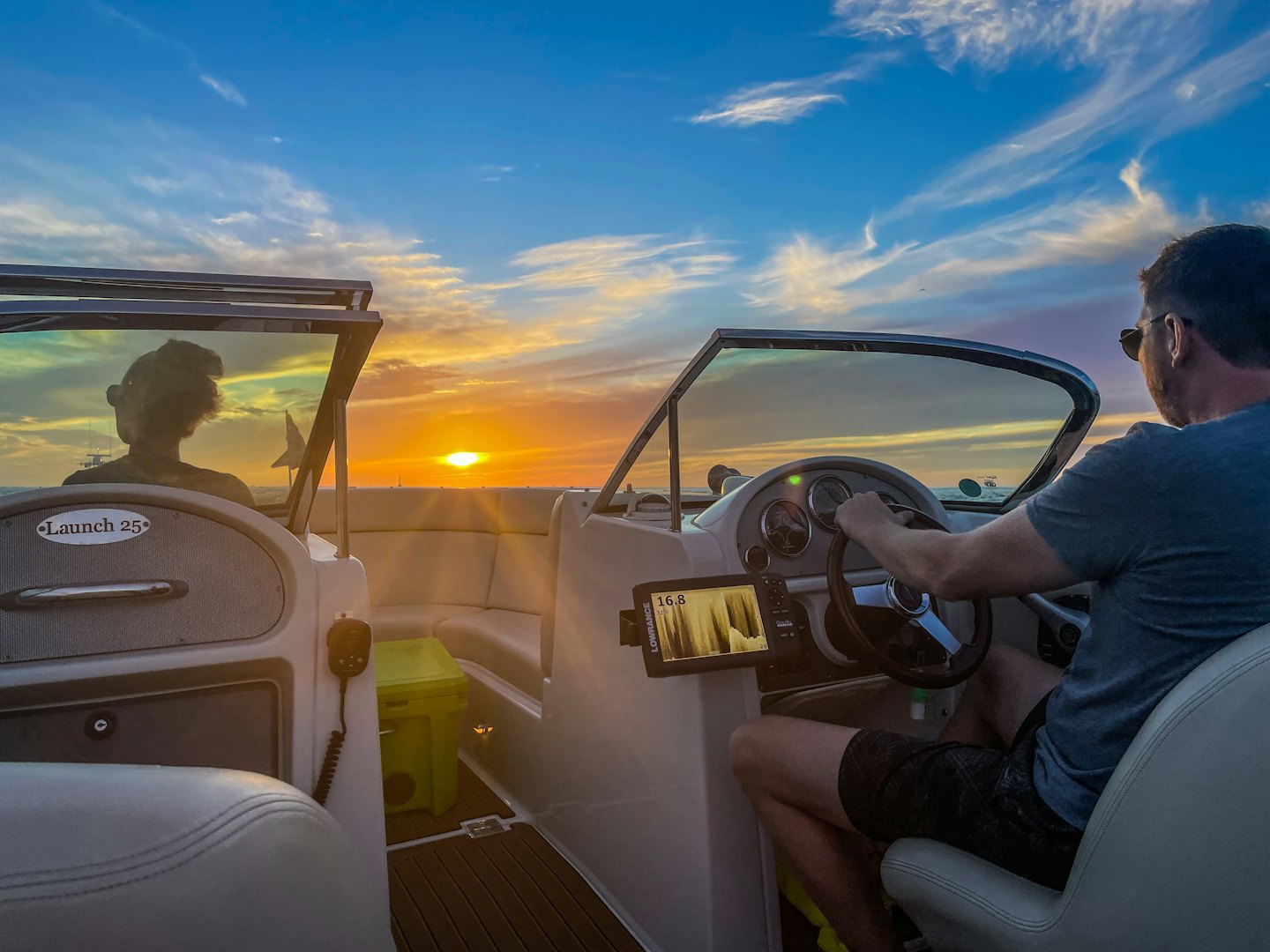 Two people steer a boat across the water at sunset.