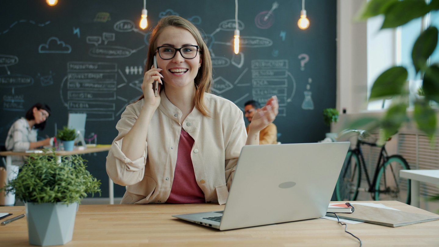 Donna con occhiali parla al telefono in un ufficio moderno.