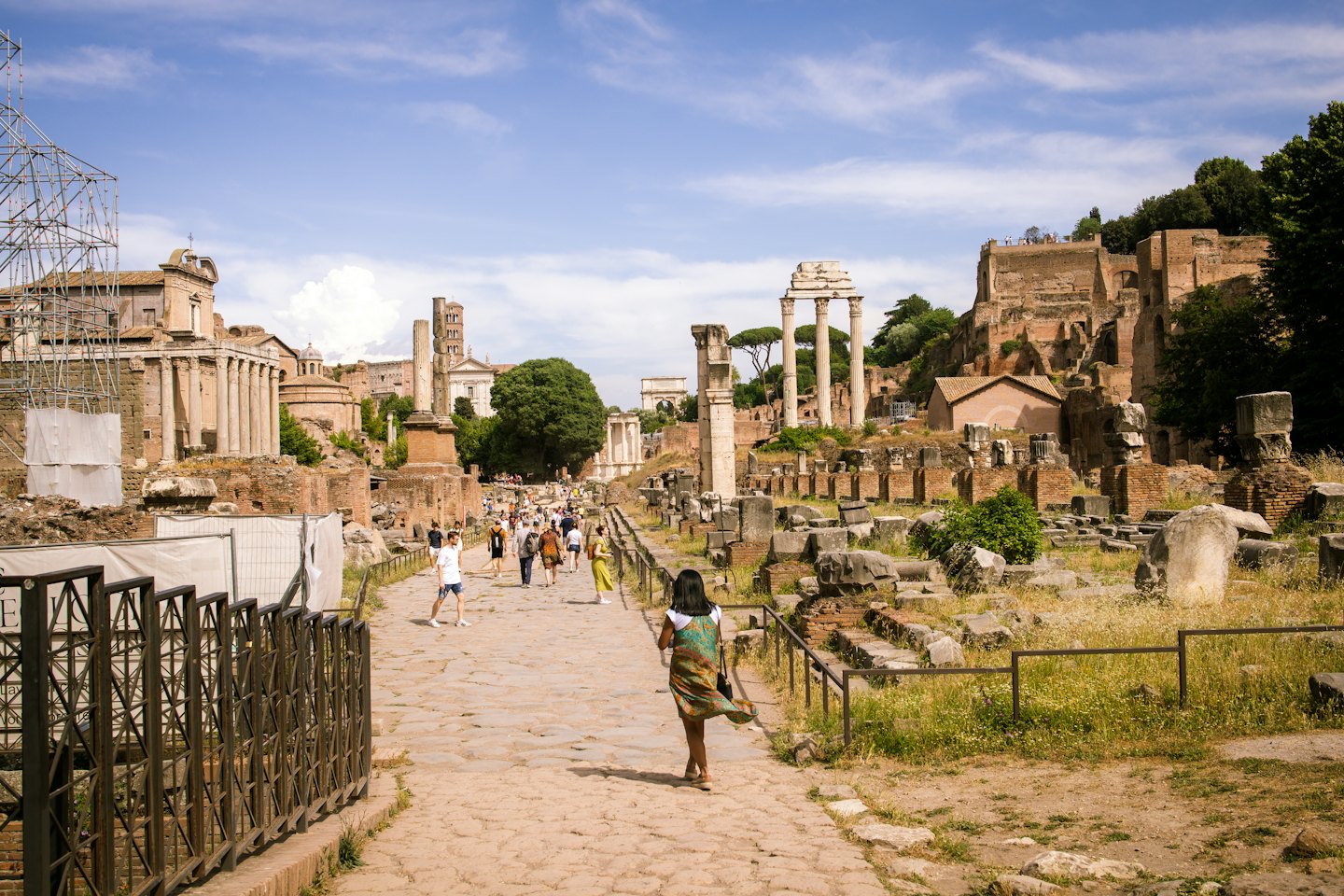 Tourists walk along a stone path through ancient Roman ruins.