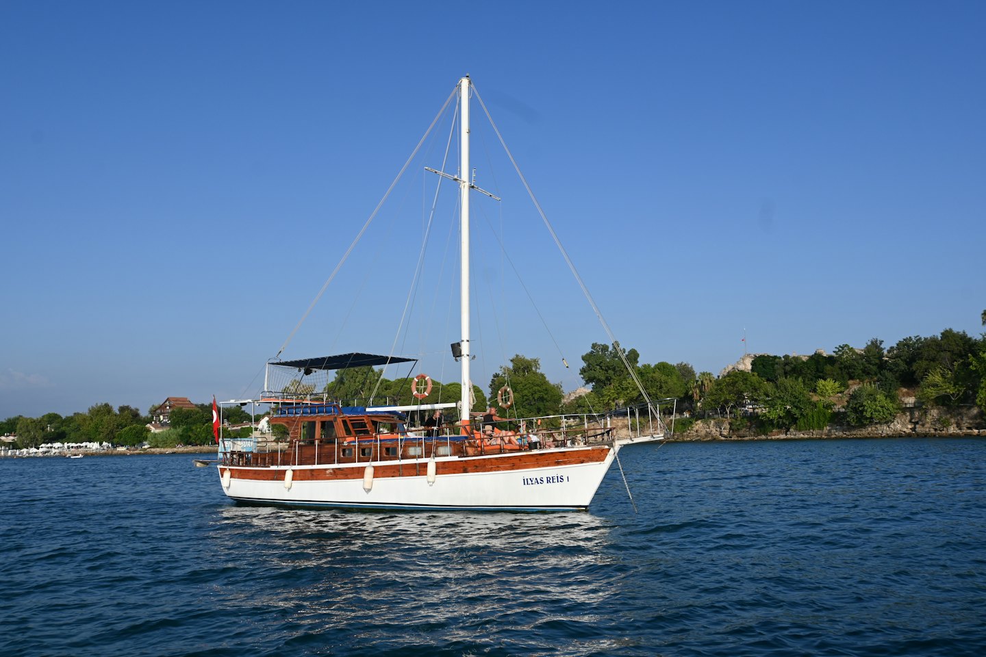 People lounge on a wooden boat near a lush coastline.
