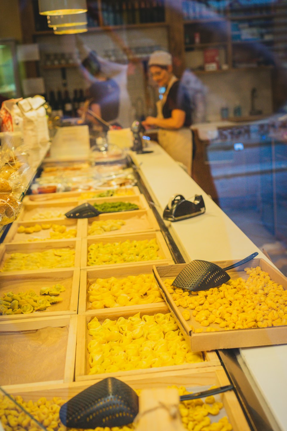Pasta gialla e verde esposta in vassoi di legno dietro un bancone di vetro.