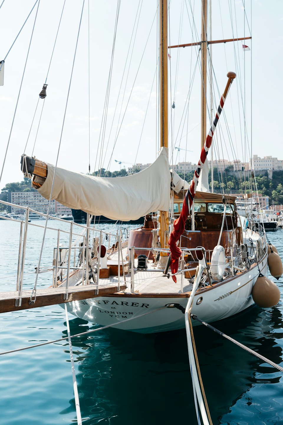 Barca a vela di legno ormeggiata in acque limpide vicino a una città costiera.