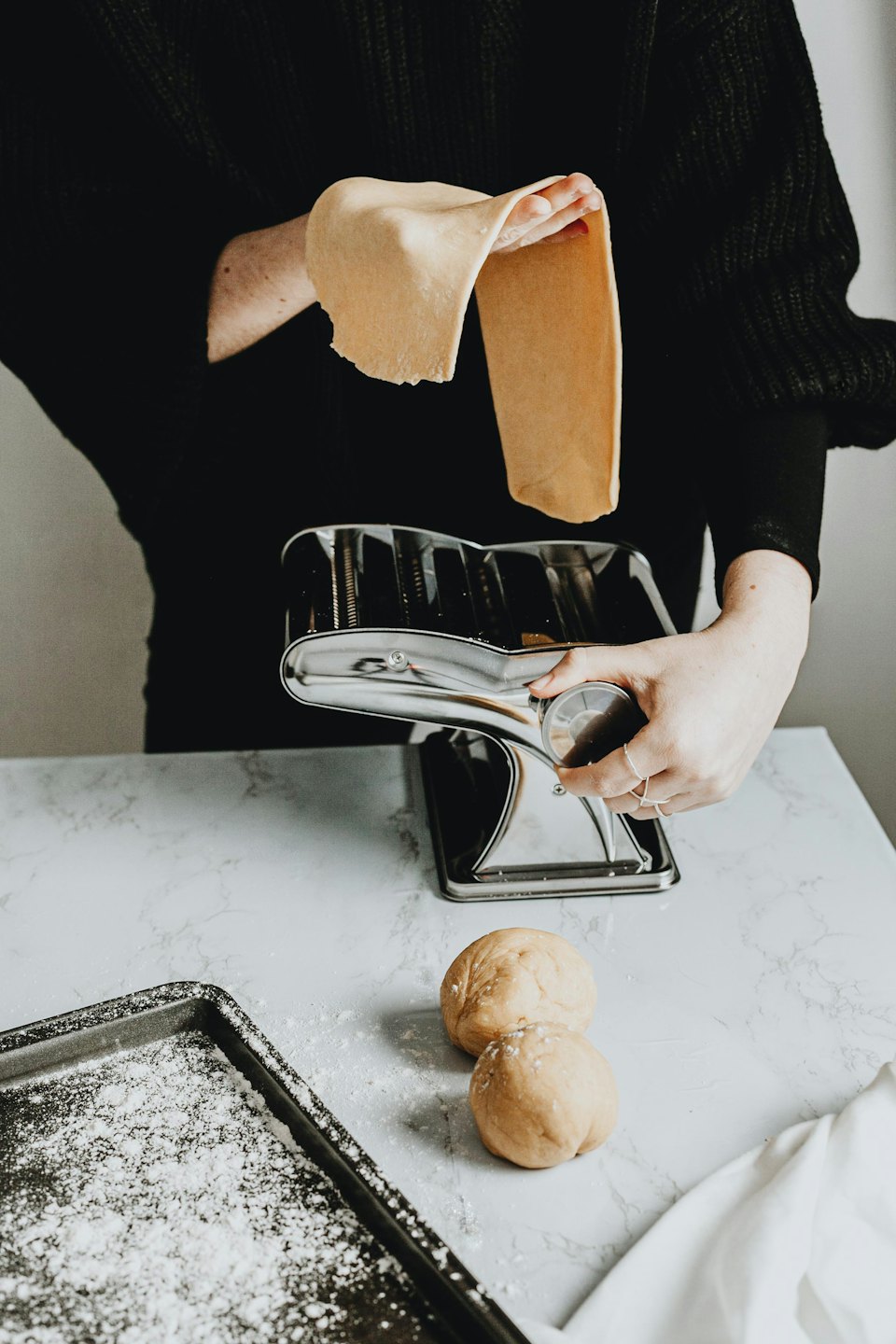 Hands shaping fresh pasta dough with a pasta maker.
